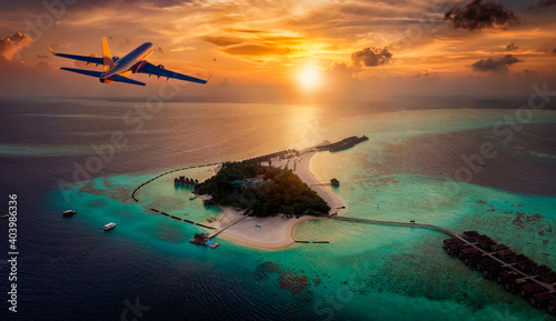 Travel concept with an airplane flying towards a tropical paradise island in the Maldives during sunset time