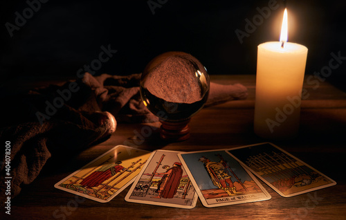 concept of fortune-telling wooden table and white candle with a crystal ball and tarot cards on dark background 
