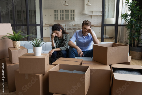 Tired unhappy young Caucasian couple sit on sofa in new living room feel unmotivated unpacking. Upset stressed millennial man and woman have fight quarrel unboxing packages relocating moving.