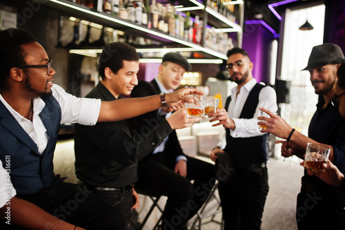 Cheers! Group of handsome retro well-dressed man gangsters spend time at club. Drinking whiskey at bar counter. Multiethnic male bachelor mafia party in restaurant.