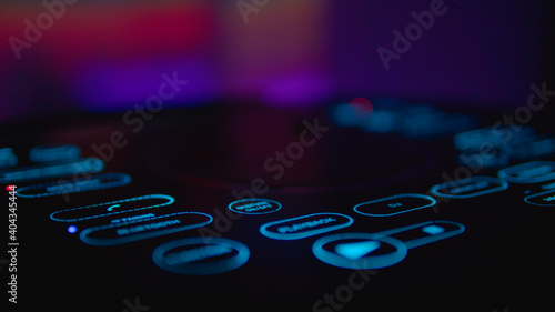 Podświetlona stacja DJ, w tle ciepłe, imprezowe kolory. Błękitne, smukłe przyciski urządzenia.