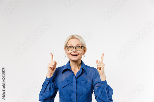 Blonde confident smiling employee business woman 40s wear blue classic shirt glasses formal clothes point index fingers overhead on copy space mock up isolated on white background studio portrait