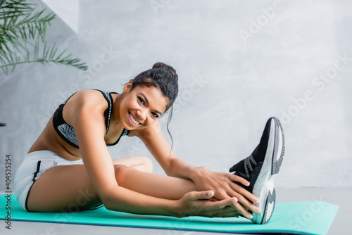 cheerful african american woman looking at camera while stretching on fitness mat at home