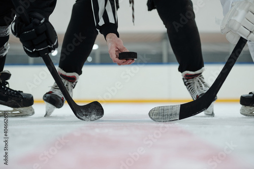 Hand of referee holding puck over ice rink with two players standing around him