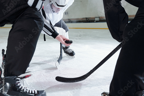 Hockey referee holding puck over ice rink while two rivals with sticks around