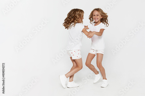 Smiling funny little twin sisters in white clothes dancing isolated on white background children studio portrait.