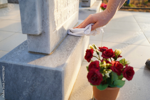 Cleaning cemetery. A woman's hand washes grey monument at the grave with rag