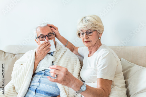 Woman checking fever temperature of senior man. Old husband resting at home feeling sick while his wife checking fever by touching forehead