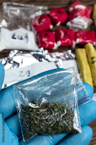 evidence of smuggling traffic: Packaging of a narcotic substance in the hand of a forensic expert against the background of other arrested materials, cocaine, heroin, spice