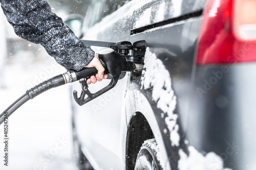 Male hand holding fuel pistol during gasoline refill in his minivan in cold winter