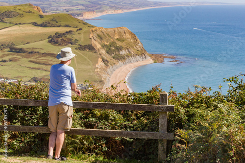 Person takes in the view out to sea from the top of Golden Cap in West Dorset, England, with background view of Bridport sandstone cliffs and Chesil beach