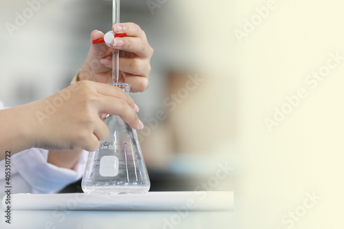 Scientist is holding burette and erlenmeyer flask. free space on right. Focus on finger holding burette.