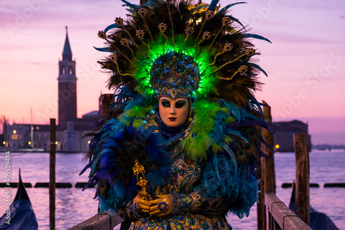 Venice, Italy - February 19, 2020: An unidentified woman in a carnival costume in front of a group of gondolas and St Giorgio's Island, attends at the Carnival of Venice.