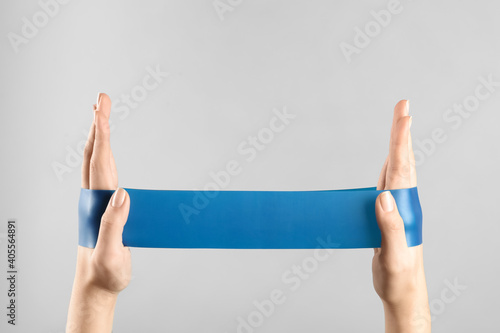 Woman with fitness elastic band on light grey background, closeup