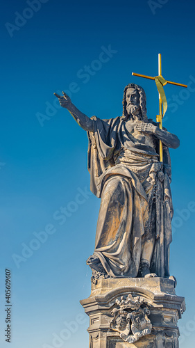 Statue of saint with cross at the Charles Bridge in Prague at blue gradient sky, Czech Republic, summer time