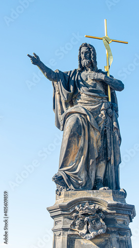 Ancient statue of a saint monk with a cross at the Charles Bridge in Prague at blue sky and copy space, Czech Republic, summer, closeup