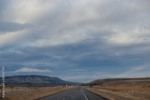 Autumn landscape at dusk. Asphalt road among steppes with yellow dry grass, blue mountains on the horizon, beautiful blue-gray autumn sky. Montana, USA, 11-23-2019