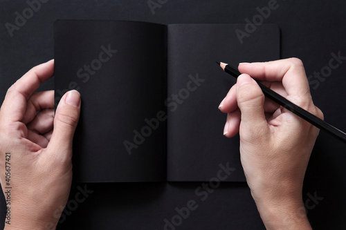 Manos escribiendo en una libreta negra con un lápiz negro sobre un fondo negro. Espacio libre para texto.