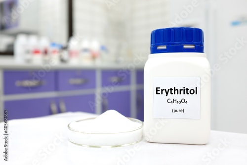 Selective focus of a bottle of pure erythritol sugar substitute artificial sweetener with powder in petri dish. White laboratory background with copy space.