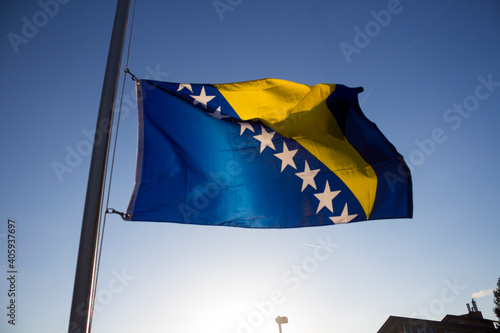 A Bosnian flag on a pole waves in the wind on a sunny day.