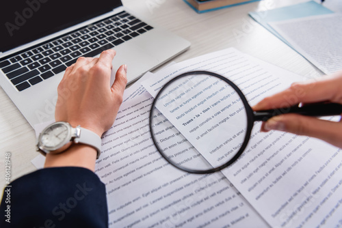 cropped view of translator holding magnifier glass near documents with english text, blurred foreground