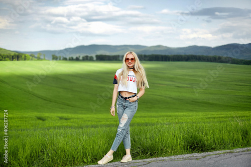 Beautiful blonde model girl in jeans and t-shirt walking by the lonely road in the countryside