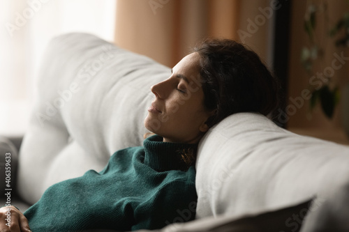 Calm young woman sit rest on cozy sofa at home sleep or take nap doing lazy weekend indoors. Millennial female relax on couch in living room daydream relive negative emotions. Stress free concept.