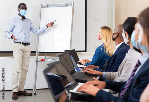 Side view of a group of businessmen in protective masks undergoing training under the guidance of a teacher