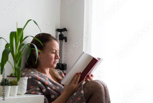 Woman in a bathrobe and nylons reading a book during the lockdown period. Quarantine inside an apartment.