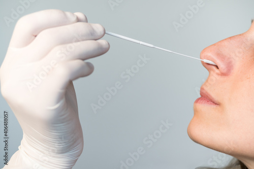 A nurse wearing latex gloves inserts a swab into a woman's nose to collect a possible positive COVID-19 sample during the pandemic. Antigen test procedure.