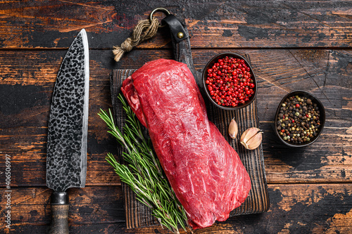 Whole Raw Tenderloin veal meat for steaks fillet mignon on a wooden cutting board with butcher knife. Dark wooden background. Top view