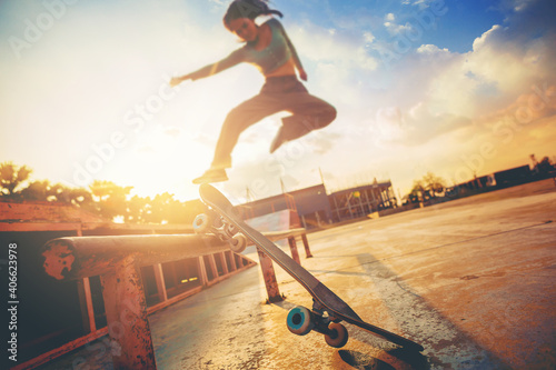 Young woman practising skateboarding at skate park. Women try to playing skateboard jumping at the roll bar with sunset background.