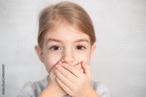 portrait of little girl, child closing his mouth with hands. Speech therapist, speech problems, stammering, mumbling.