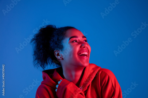 Happiness, cheerful. African-american woman's portrait on blue studio background in red-pink neon light. Beautiful female model. Concept of human emotions, facial expression, sales, ad, fashion.