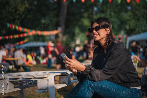 Beautiful female using mobile phone on sunny day on outdoor street fair parade festival