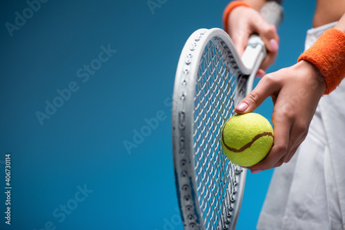 partial view of sportive young woman holding tennis racket and ball while playing on blue