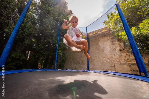 Little happy toddler girl jumping on her trampoline outside on a summer day. Kid jumping on trampoline. 