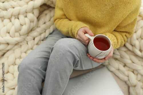 Woman with cup of tea sitting near plaid, closeup