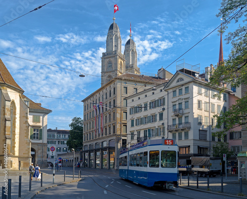 A blue tram traveling through downtown Zurich with the towers of the Grossmunster church above the buildings