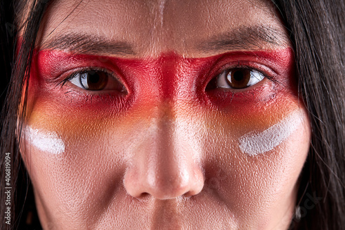 close-up eyes of indian woman confidently looking at camera, serious ethnic female with paintings on face. indian ehnicity, shaman concept