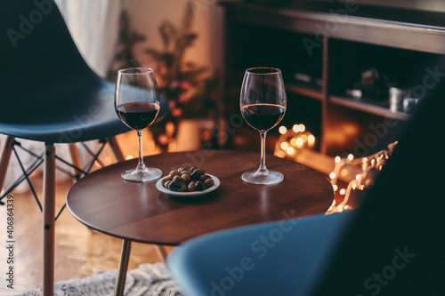 Two glasses of red wine and olives on a table, cosy room with candid lights, concept of romantic evening