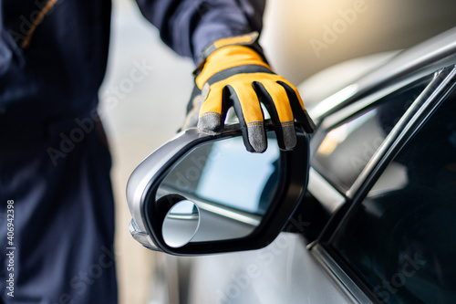 Male auto mechanic hand wearing yellow glove adjusting car wing mirror. Checking car part in automotive industry. Automobile servicing and repair concept