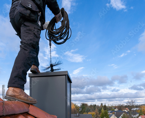 Chimney sweep man in work uniform cleaning chimney on building roof