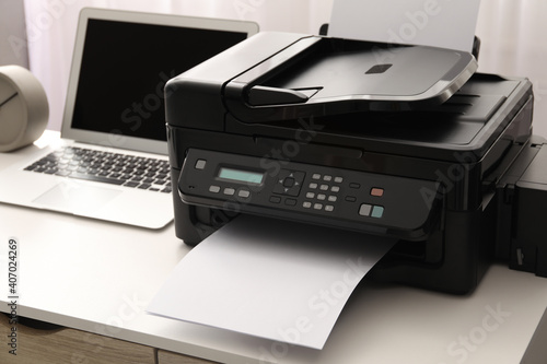 Modern printer and laptop on white table indoors