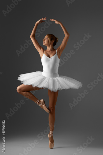 graceful ballerina in white tutu and pointe shoes on gray background