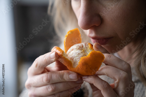 Sick woman trying to sense smell of fresh tangerine orange, has symptoms of Covid-19, corona virus infection - loss of smell and taste, standing at home. One of the main signs of the disease.