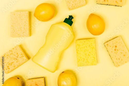 Top view of whole lemons near sponges and dishwashing liquid on yellow background