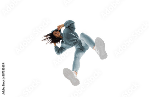 Dancing. Young stylish woman in modern street style outfit isolated on white background, shot from the bottom. Caucasian fashionable model in shoes and overalls, musician, rapper performing.