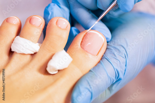 Close up of professional painting french pedicure nails on foot. Specialist in beauty salon making french pedicure for female client. Relaxing at beauty salon, caring about nails. 