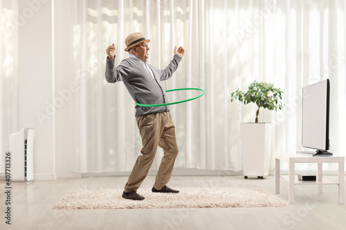 Elderly gentleman spinning a hula hoop in front of tv in a minimal modern living room